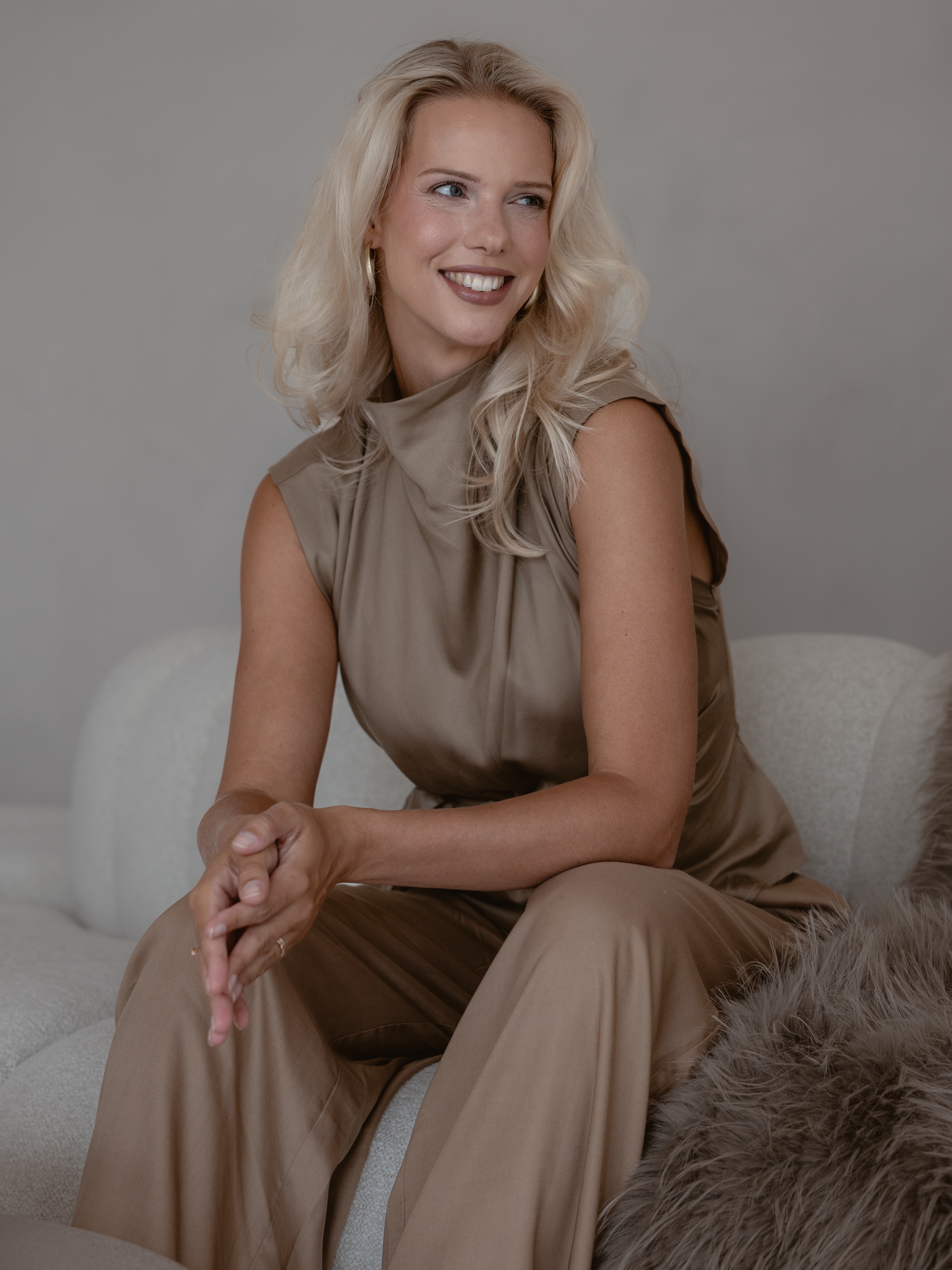 Vrouw in een taupekleurige outfit op een stoel in de studio